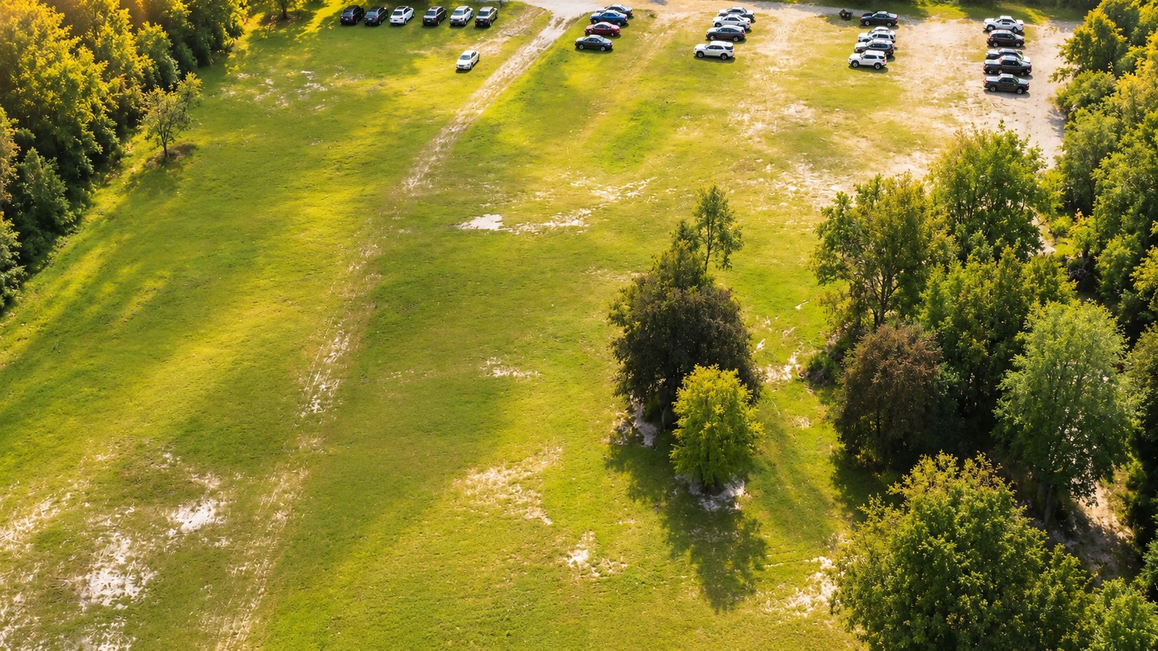 Enhanced aerial view of the open lawn, wooded surroundings and on-site parking